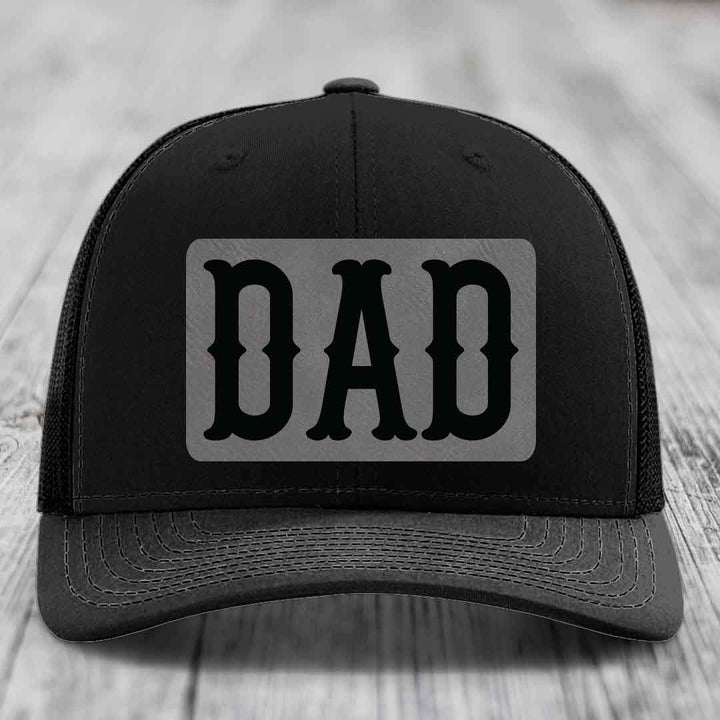 Tan and blue trucker hat with a grey leatherette patch that says DAD in black letters.