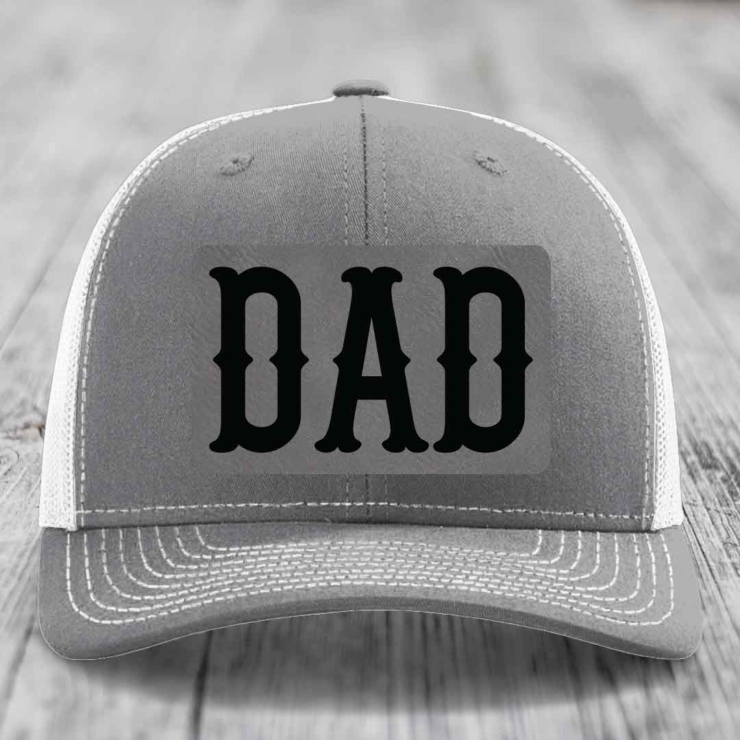 Pink trucker hat with black mesh back and gray leatherette patch that says DAD in black letters.