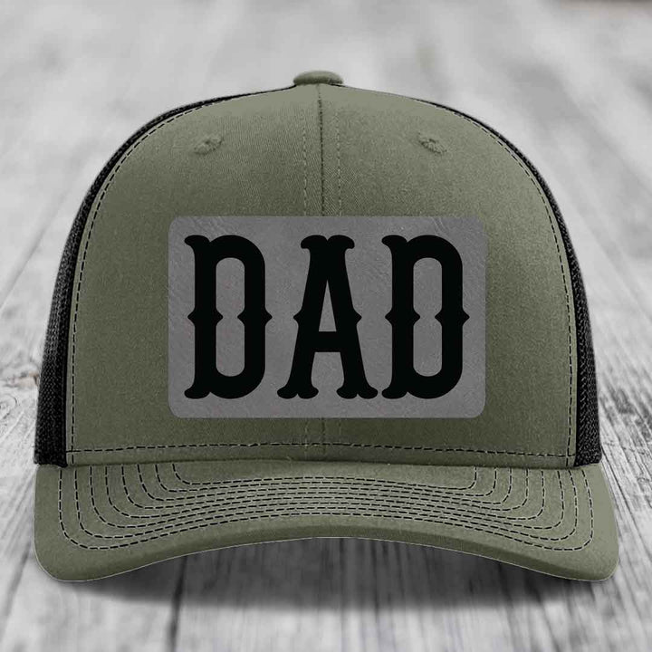 Black trucker hat with a grey leatherette patch that says DAD in black letters.