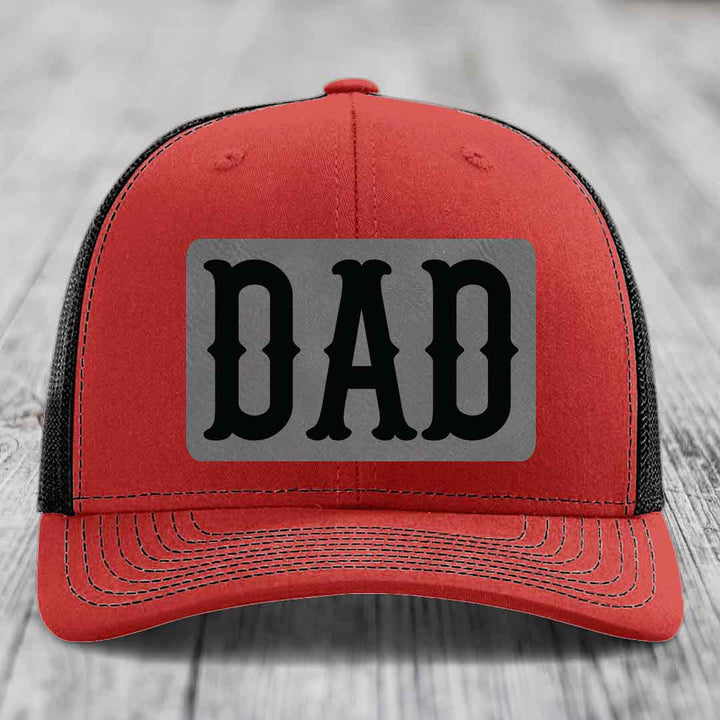 Blue trucker hat with black mesh back and gray rectangular patch that says DAD in black letters.