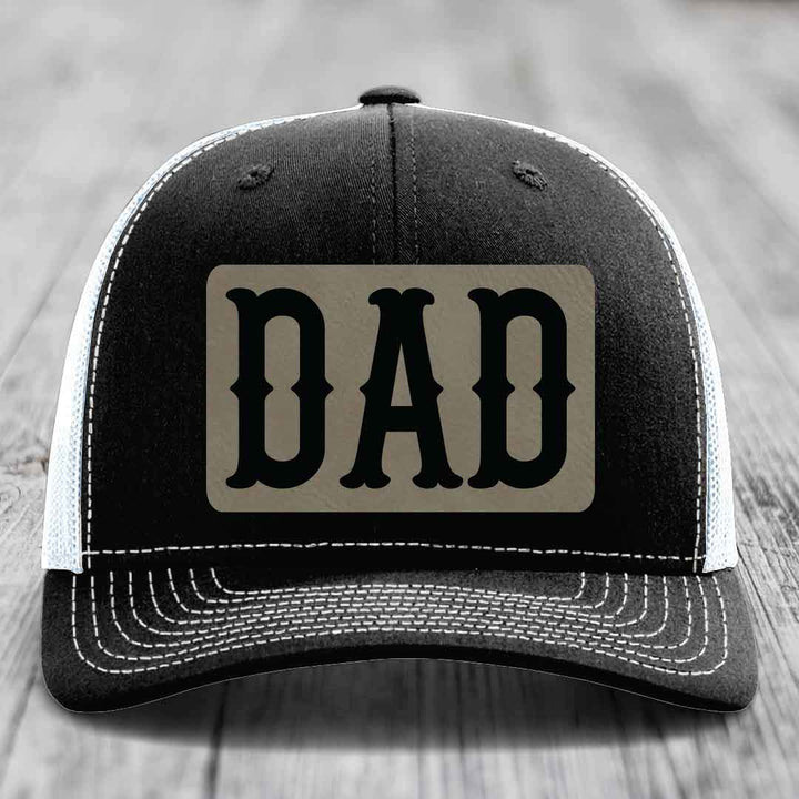 Black and white trucker hat with a beige leatherette patch that says &