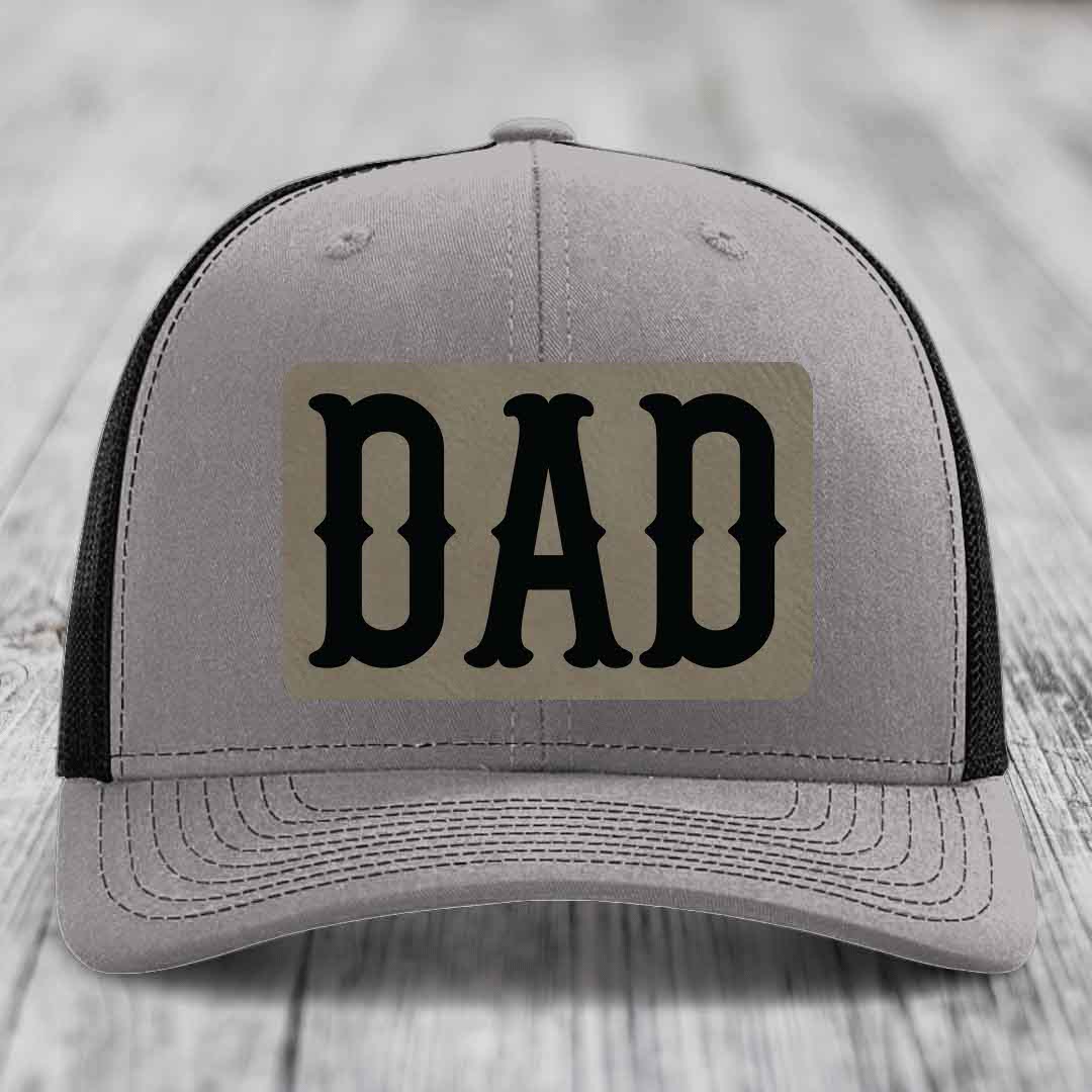 Grey trucker hat with blue mesh sides and a beige leatherette patch that says DAD in black letters.
