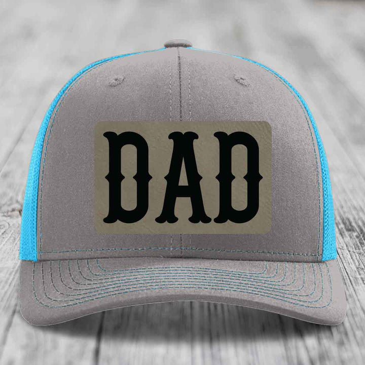 Grey trucker hat with neon green mesh and stitching, featuring a beige leatherette patch with black &