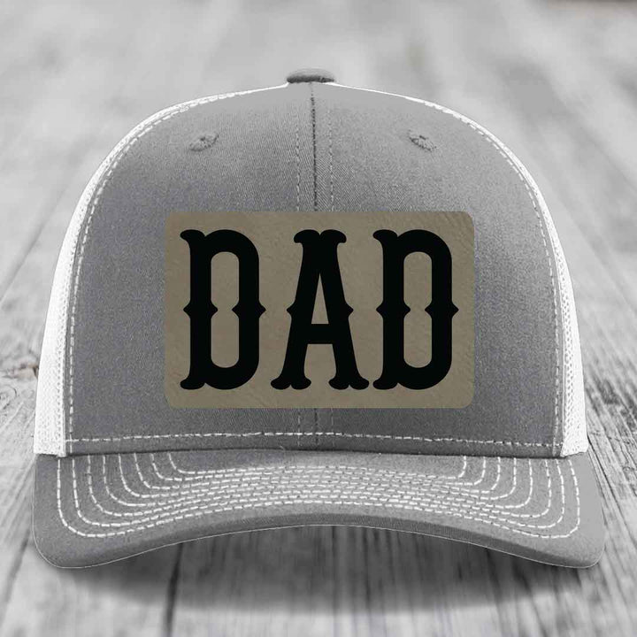 Pink trucker hat with black mesh back and gray leather patch that says DAD in black letters.