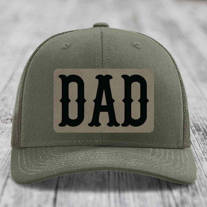 Olive green trucker hat with black mesh back and a beige leatherette patch that says &