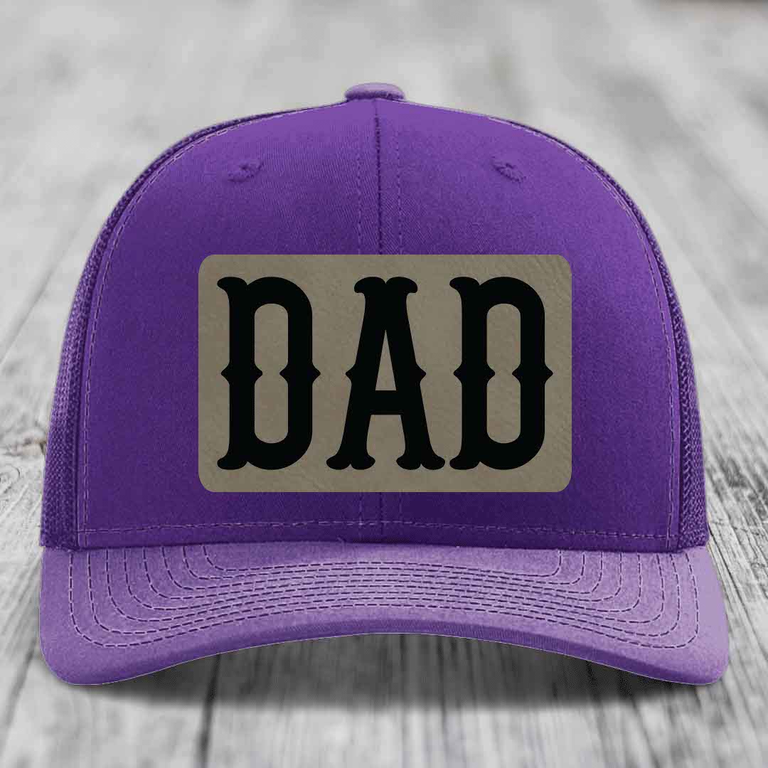 Red trucker hat with black mesh back and gray leather patch that says DAD in black letters.