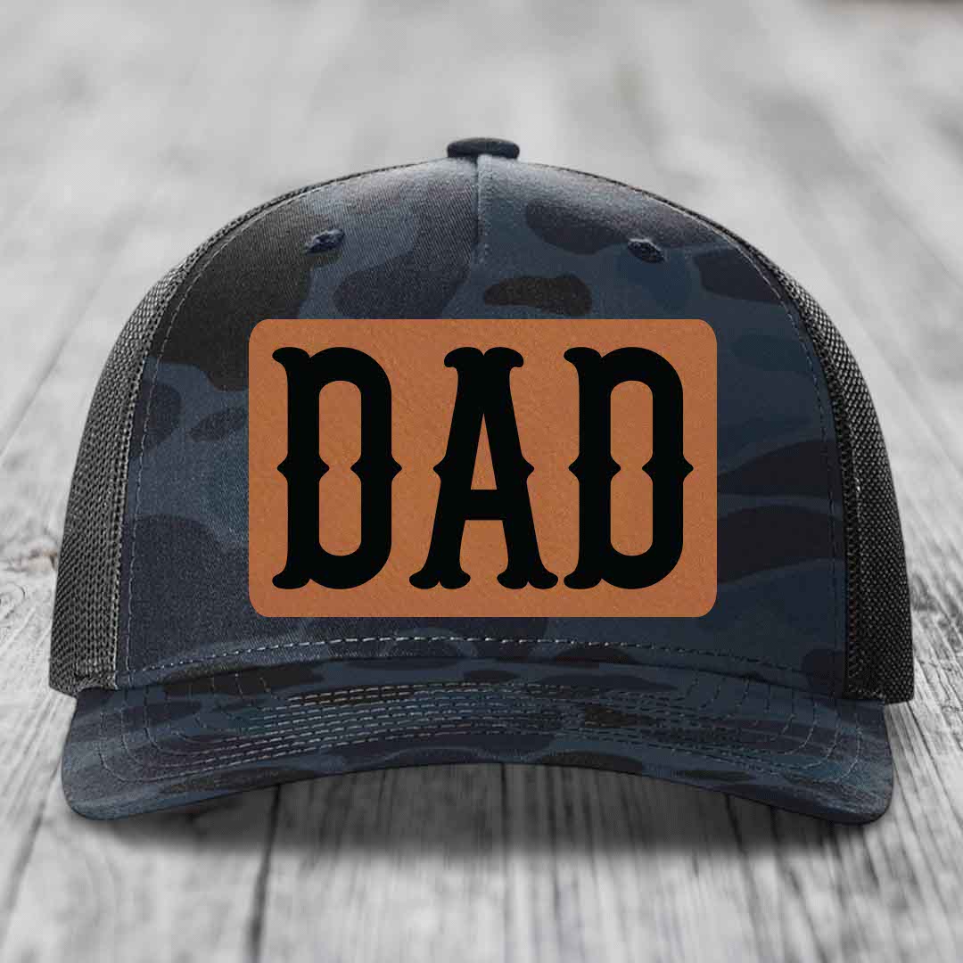 Camouflage trucker hat with brown leather patch that says DAD in black letters.