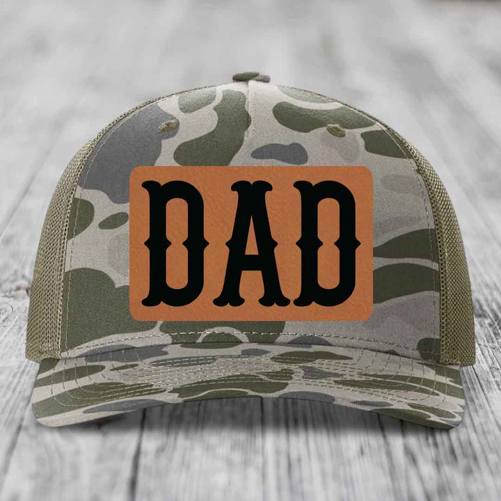 Camouflage trucker hat with brown leather patch that says DAD in black letters.