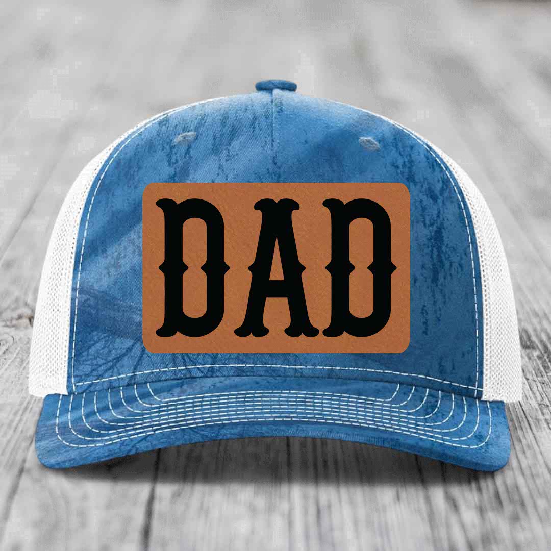 Camouflage trucker hat with brown leather patch that says DAD in black letters.