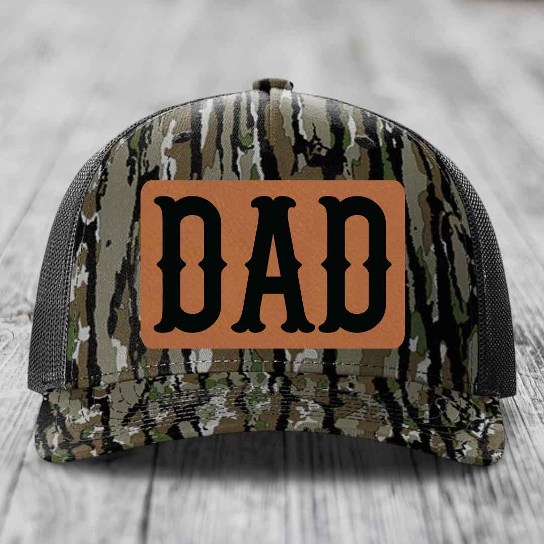 Black camouflage trucker hat with brown leather patch that says DAD in black letters.