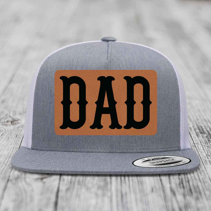 Grey and white trucker hat with brown leather patch that says DAD in black letters.
