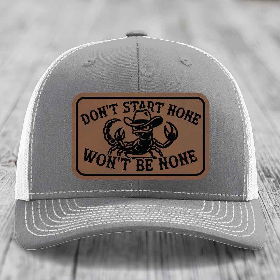 Grey trucker hat with brown leather patch featuring a scorpion in a cowboy hat and the text &