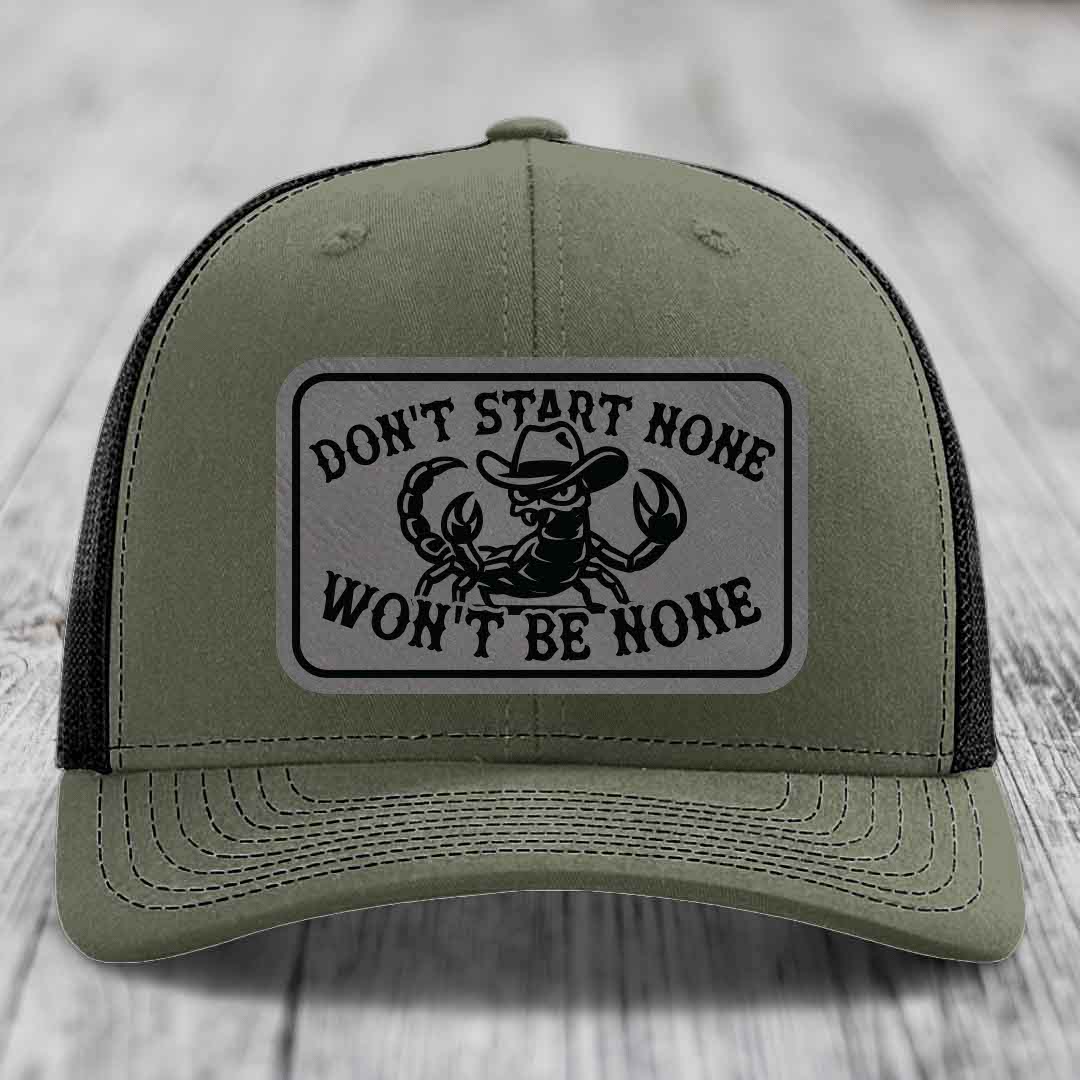 Olive green trucker hat with black mesh back and a rectangular leather patch featuring a scorpion wearing a cowboy hat and the text &