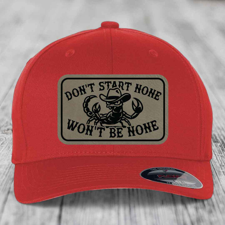 Red baseball cap with beige leather patch featuring a scorpion in a cowboy hat and the text &