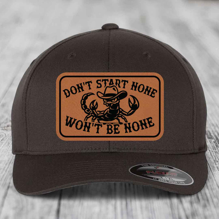 Dark brown baseball cap with tan leather patch featuring a scorpion in a cowboy hat and the text &