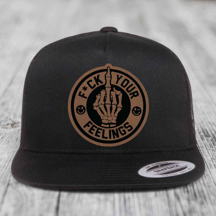 Black trucker hat with circular tan leatherette patch showing skeleton hand and text &