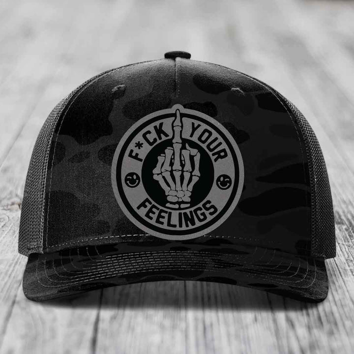 Black camouflage trucker hat with a circular patch featuring a skeleton hand and the text &