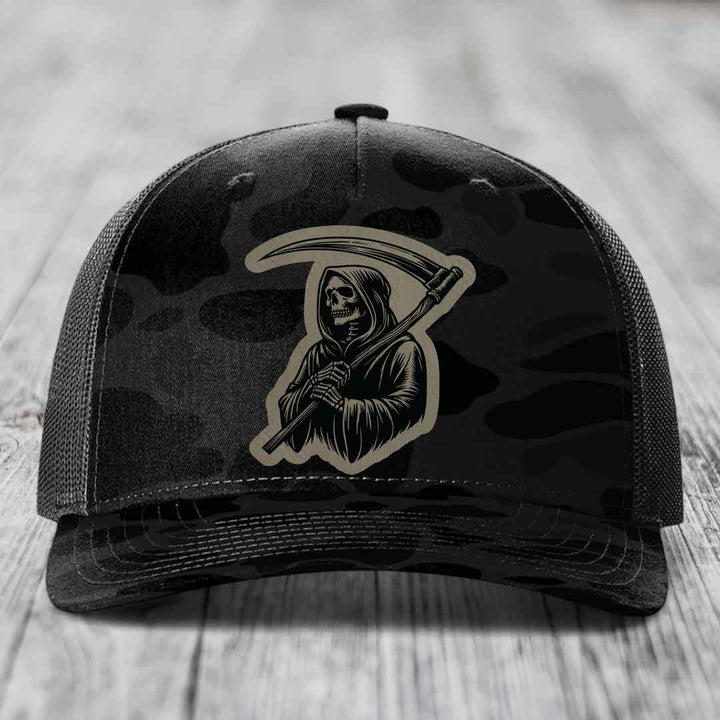 Black camouflage trucker hat with a beige Grim Reaper patch on the front.