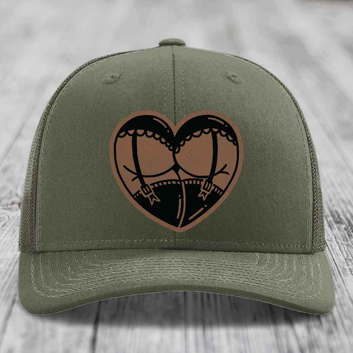 Olive green trucker hat with heart-shaped leather patch depicting garter belt design.