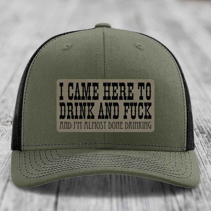 Olive green trucker hat with black mesh back and a rectangular patch reading &