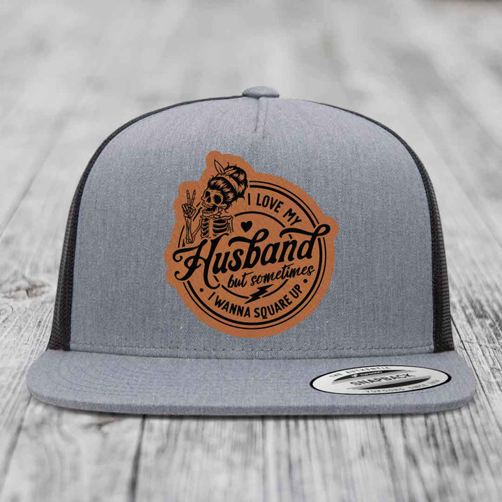 Grey trucker hat with brown leather patch featuring skeleton holding peace sign and text &
