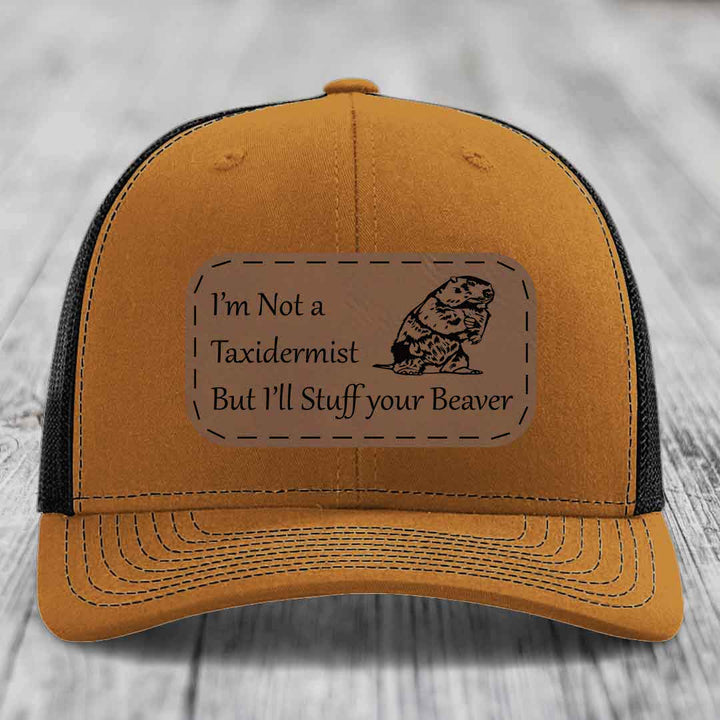 Tan trucker hat with black mesh back and a brown leather patch that reads &