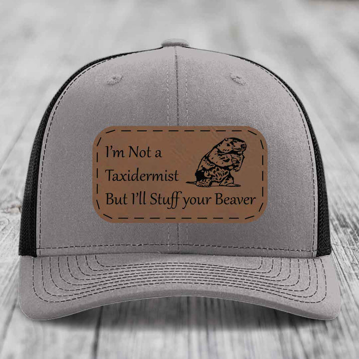 Grey trucker hat with black mesh back and a brown leather patch that reads &