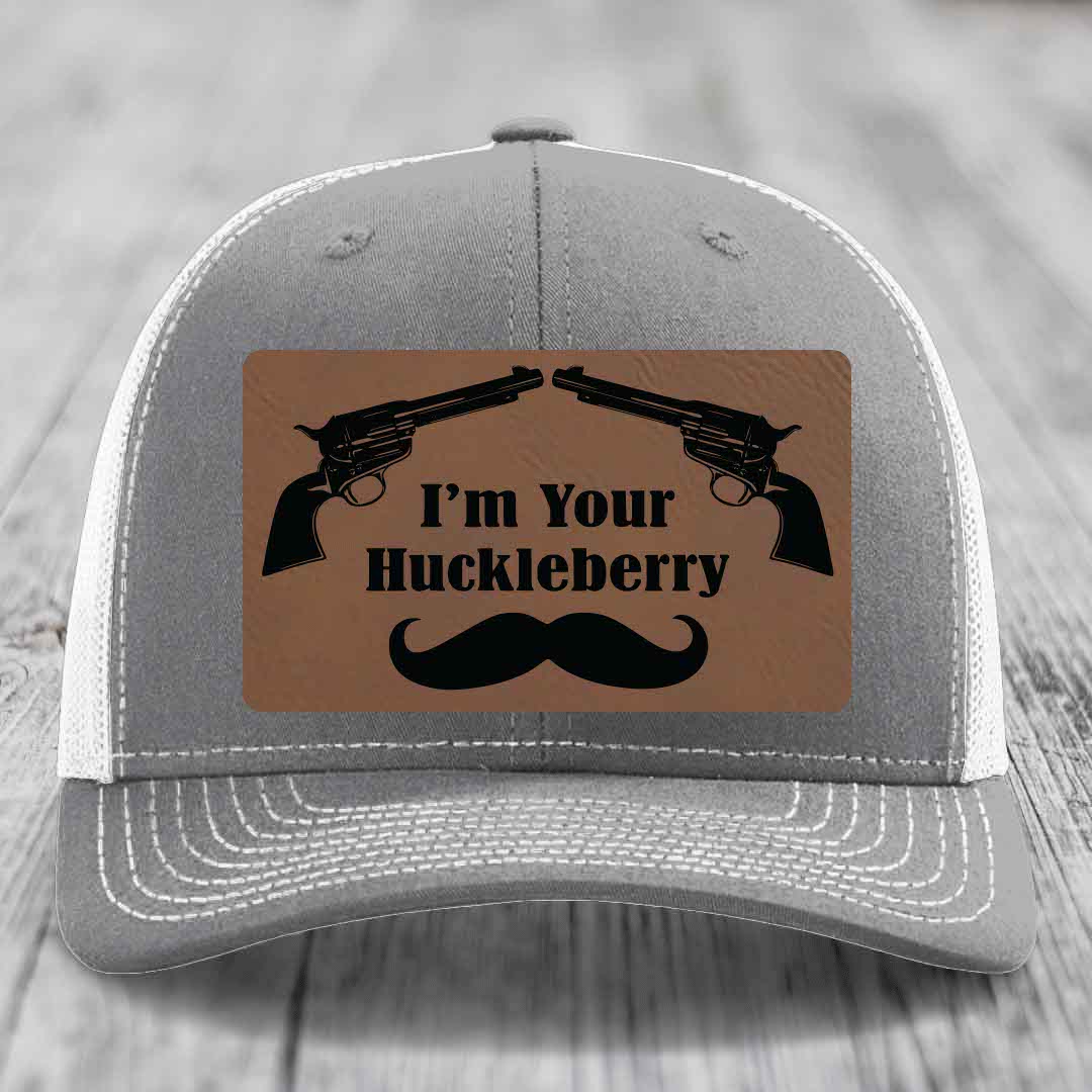 Grey trucker hat with brown leather patch featuring two revolvers, text &