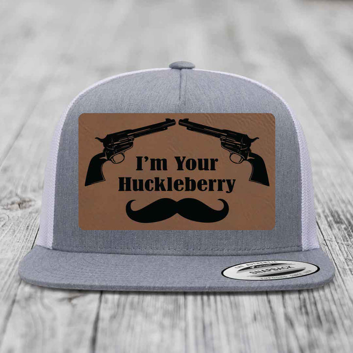 Grey trucker hat with brown leather patch featuring two revolvers, text &