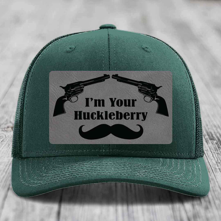 Green trucker hat with a grey leatherette patch featuring two crossed revolvers, the text &