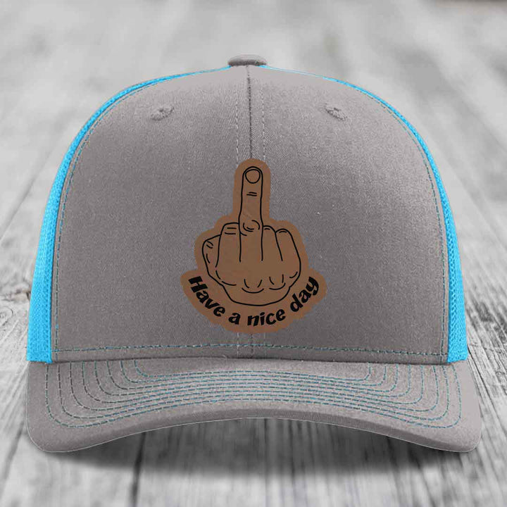 Grey trucker hat with blue mesh sides and a brown leatherette patch showing a middle finger with text &