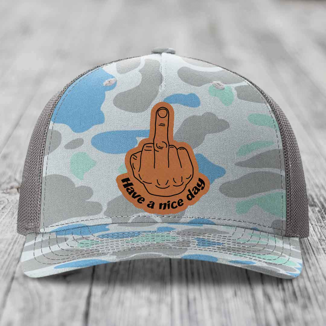 Camouflage trucker hat with brown leather patch showing middle finger and text &