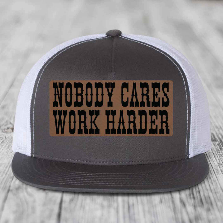 Grey front panel trucker hat with brown leather patch reading &