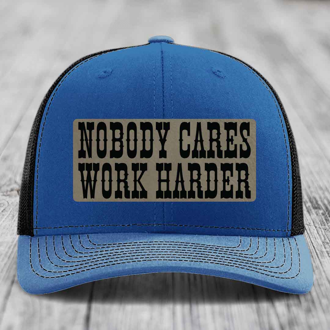 Blue trucker hat with black mesh back and a beige leather patch that reads &