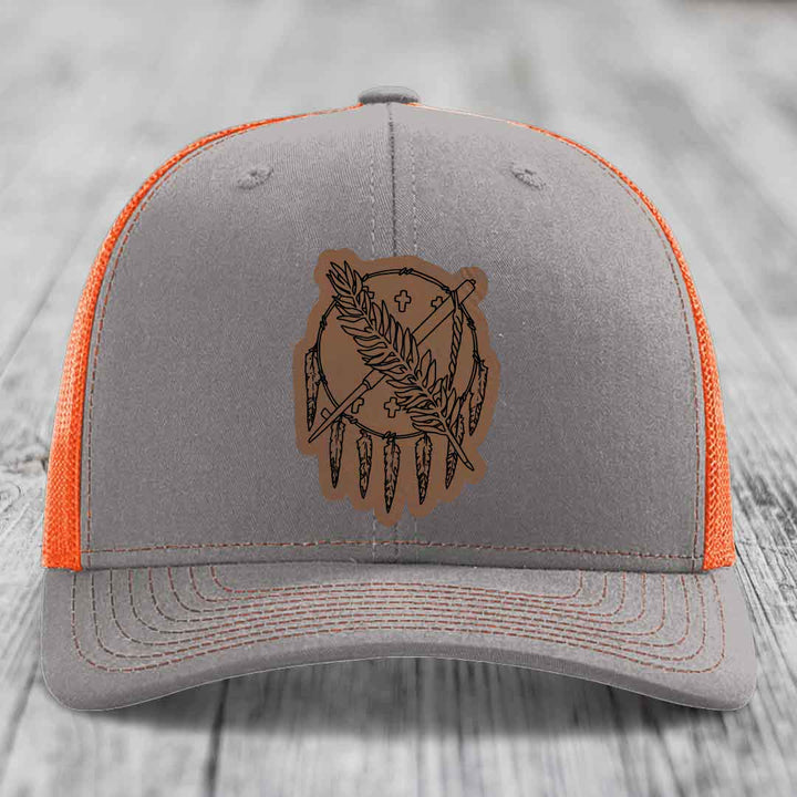 Grey trucker hat with orange mesh back and brown leather patch featuring a dreamcatcher design.