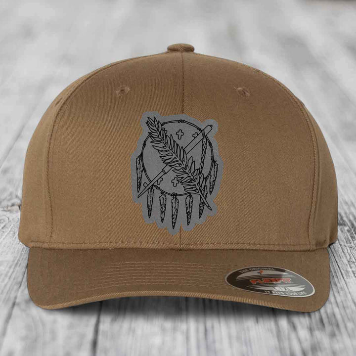 Tan baseball cap with grey dreamcatcher patch featuring feathers and crosses, Flexfit brand label visible.