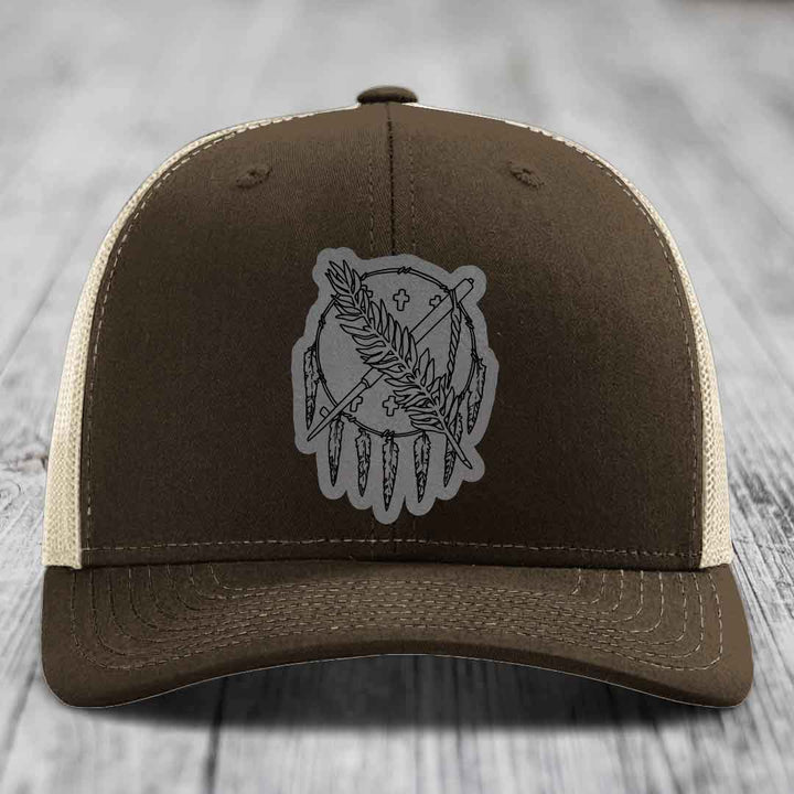 Brown trucker hat with beige mesh back and gray dreamcatcher patch on front.