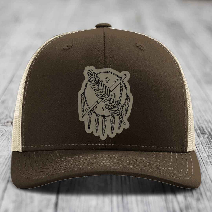 Brown trucker hat with beige mesh back and a grey leatherette patch featuring a dreamcatcher design.