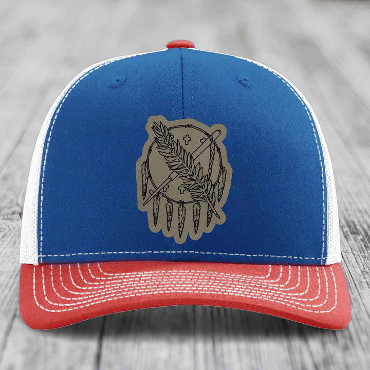Blue and red trucker hat with a beige leather patch featuring a dreamcatcher design.