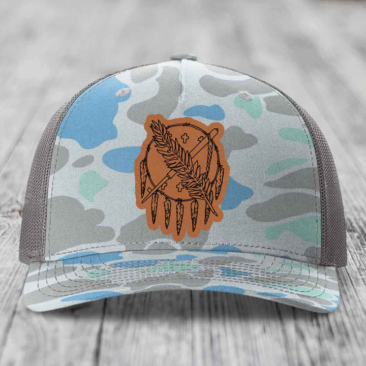 Camouflage trucker hat with brown leather patch featuring dreamcatcher design.