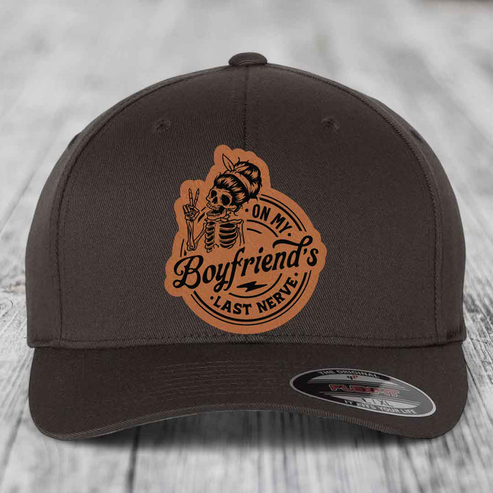 Dark brown Flexfit hat with a tan leatherette patch featuring a skeleton holding up two fingers and the text &