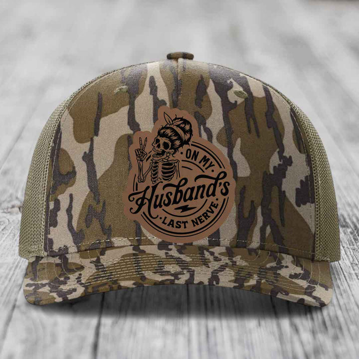 Camouflage trucker hat with a brown leatherette patch featuring a skeleton woman and the text &