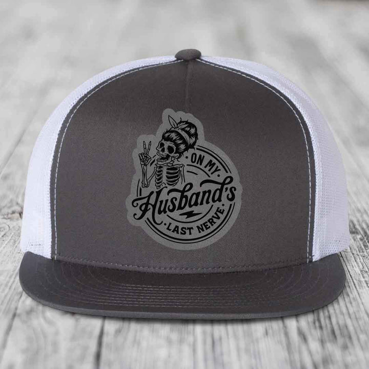 Grey and white trucker hat with black skull patch reading &