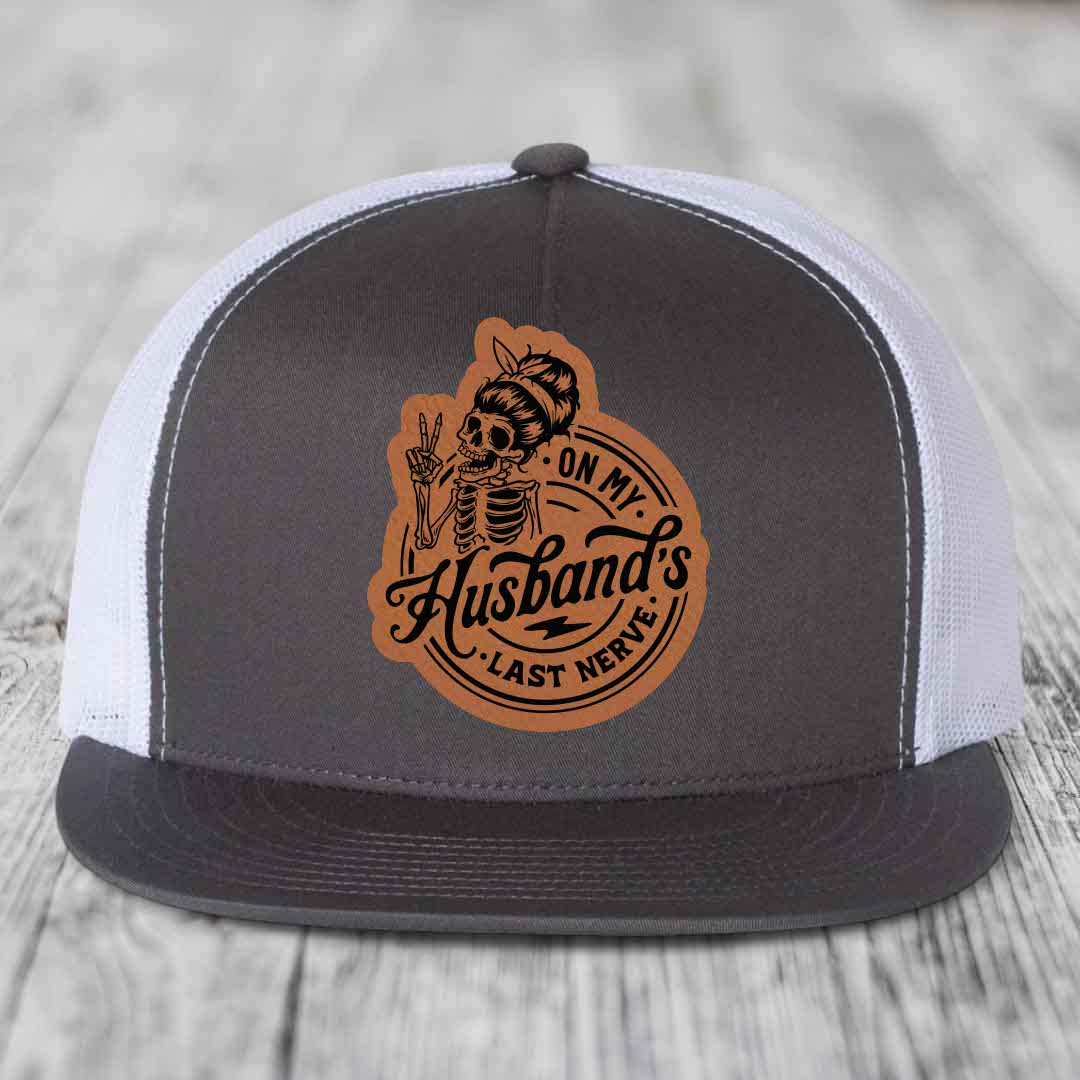 Grey and white trucker hat with brown leather patch featuring skeleton woman making peace sign.