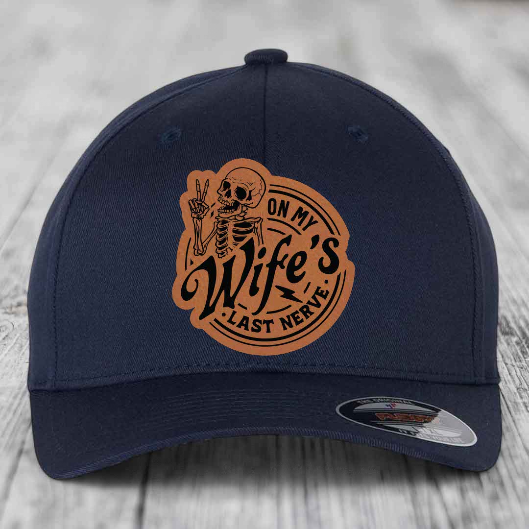 Dark blue baseball cap with a brown leatherette patch featuring a skeleton making a peace sign and the text &
