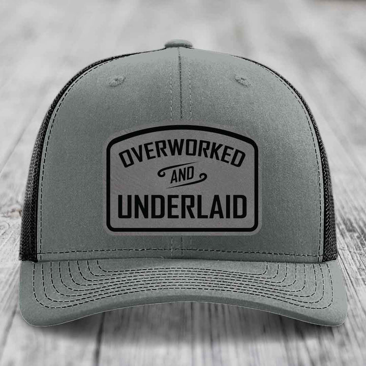 Grey trucker hat with black embroidered patch reading &
