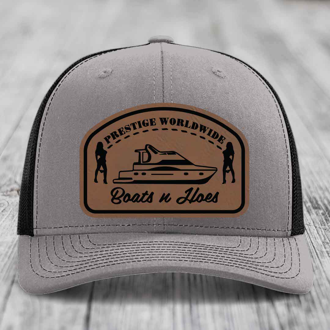 Grey trucker hat with black mesh back and brown leather patch featuring &