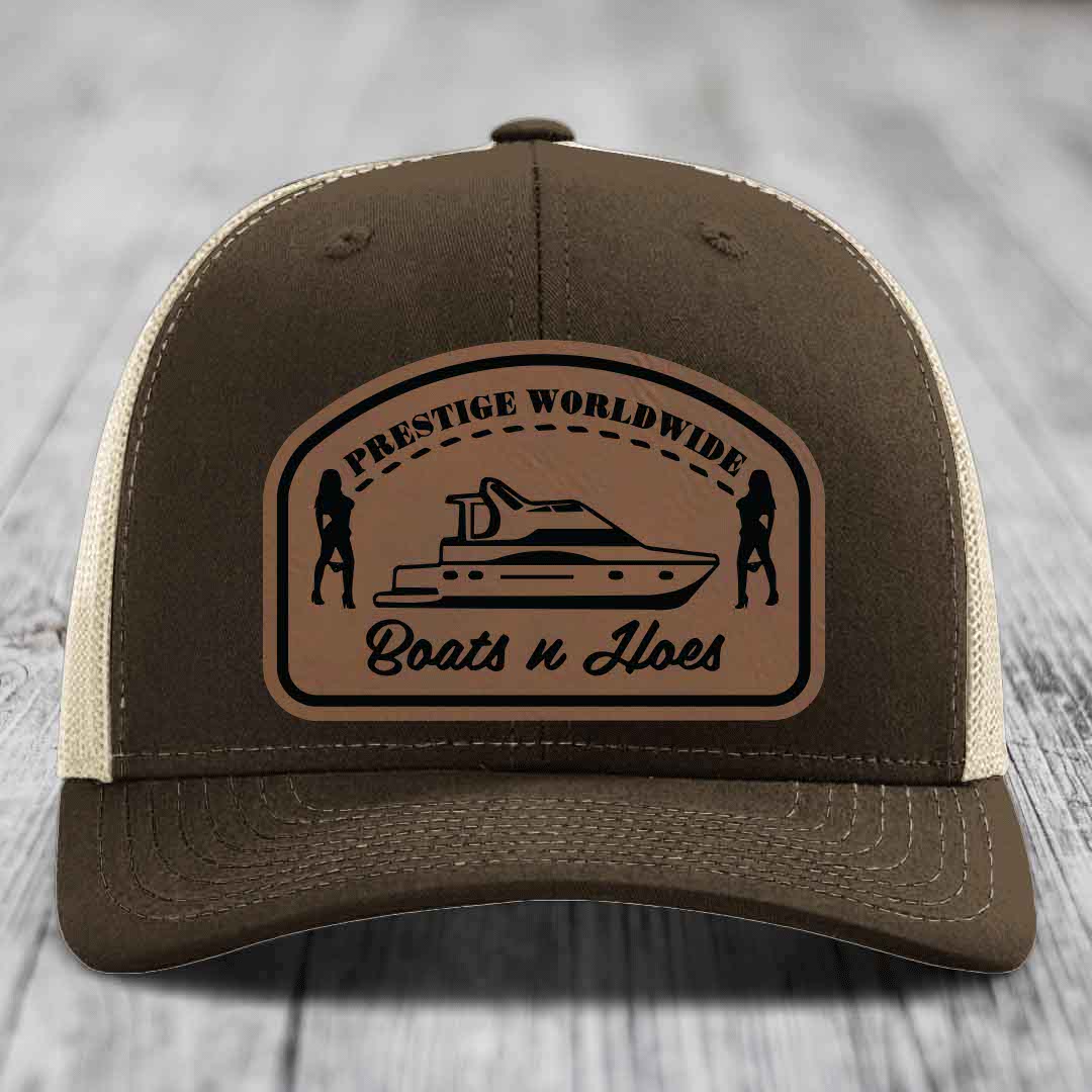 Brown trucker hat with beige mesh back and a tan leather patch featuring &
