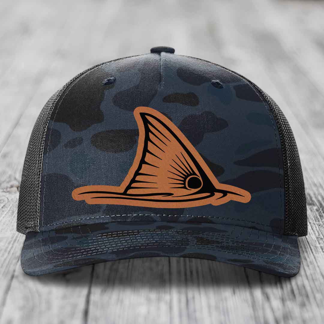 Camouflage trucker hat with orange shark fin patch on front, black mesh back.