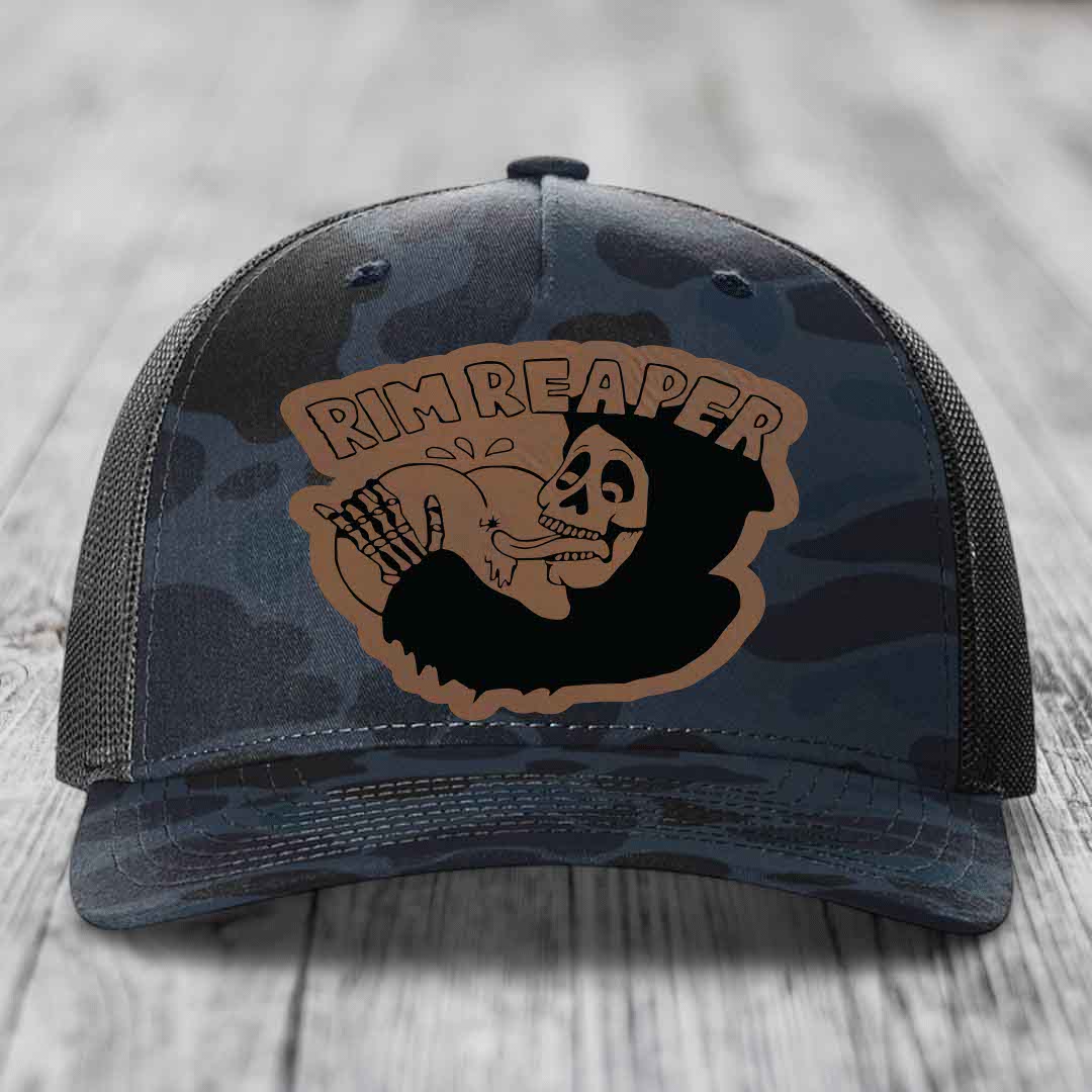 Camouflage trucker hat with brown leather patch featuring skull holding basketball and &